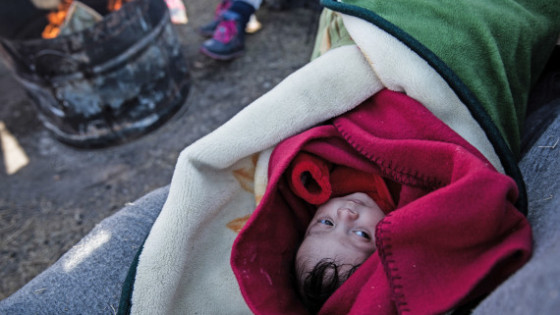 Two month old Feisal from Syria lies next to a camp fire in the yard of a petrol station in Polykastro, near Idomeni, Greece. Her father Ahmed wants to take his family to Germany.